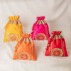 Op de afbeelding: Vier trekkoordtassen in verschillende kleuren: geel, roze, oranje en rood. Elke tas heeft gouden versieringen en ingewikkelde borduurwerk.