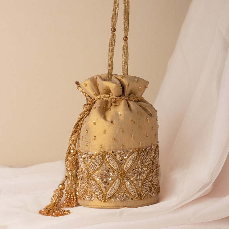 May include: A gold drawstring bag with a beaded strap and intricate embroidery. The bag has a tassel on the side and is decorated with sequins and beads.