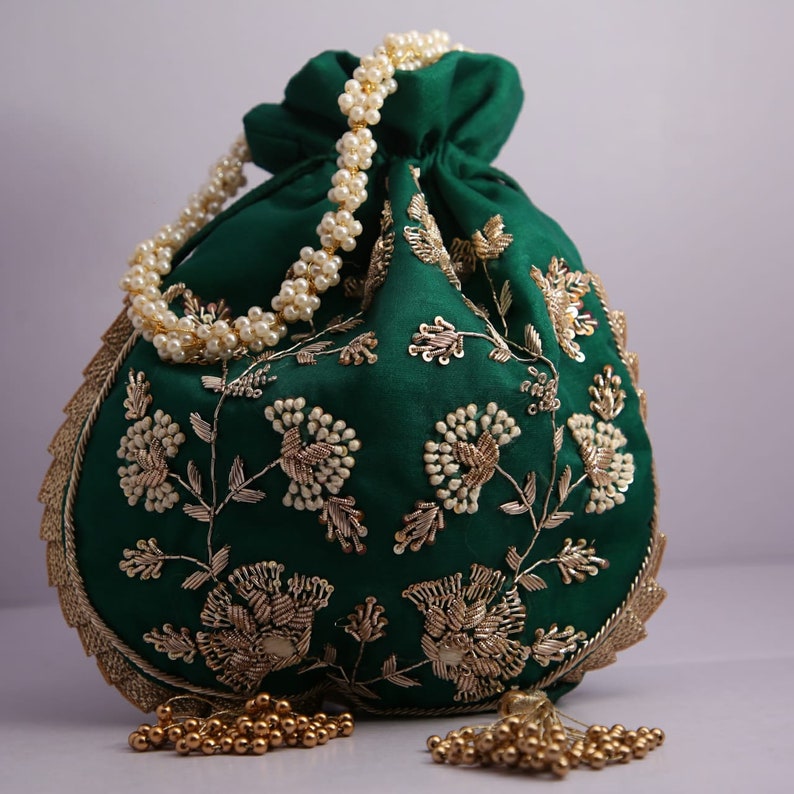 May include: A green drawstring bag with gold and white embroidery. The bag has a pearl chain handle and gold tassel accents.