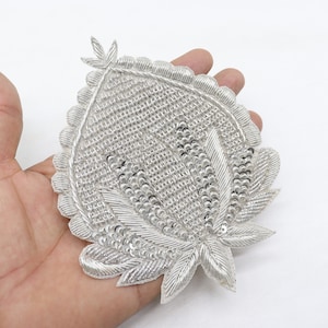 May include: A silver embroidered applique with a floral design. The applique is covered in sequins and beads.