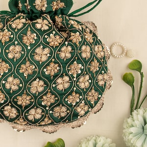 Könnte beinhalten: Eine grüne Kordeltasche mit goldener Stickerei und Pailletten. Die Tasche hat ein Blumenmuster und ist mit einem gewellten Rand verziert.