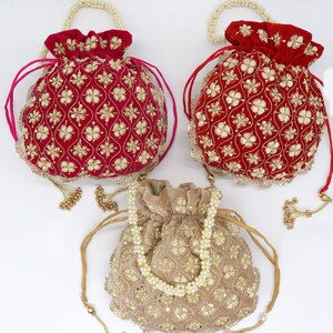 Peut inclure: Trois sacs à cordon brodés avec des embellissements décoratifs. Deux sacs sont rouges avec des broderies dorées et un sac est beige avec des broderies dorées.