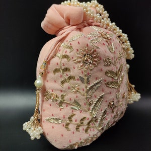 Puede incluir: Una bolsa de cord&oacute;n de terciopelo rosa con adornos dorados y de perlas. La bolsa est&aacute; decorada con bordados florales y tiene un borla de perlas.