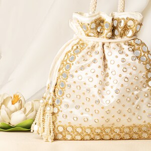 Peut inclure: Un sac à cordon blanc avec des embellissements dorés et argentés. Le sac est décoré de petits miroirs ronds et de perles. Le sac a un pompon en perles blanches.