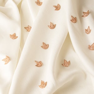 May include: White fabric with a subtle sheen, decorated with a repeating pattern of small, gold leaf-shaped embellishments.