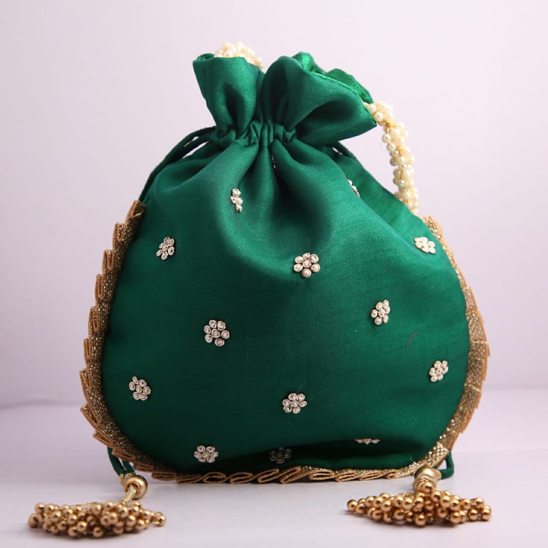 May include: A green drawstring bag with gold trim and white pearl embellishments. The bag has a gold tassel on each side.