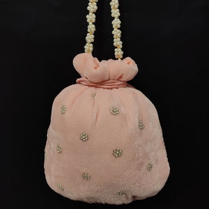 Puede incluir: Una bolsa de cord&oacute;n de terciopelo rosa con una correa de cadena de perlas y adornos dorados. La bolsa est&aacute; decorada con peque&ntilde;os acentos circulares dorados.