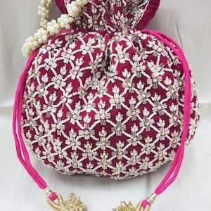May include: A pink velvet drawstring bag with a white pearl and gold bead embroidery design. The bag has a pink drawstring and gold tassel accents.