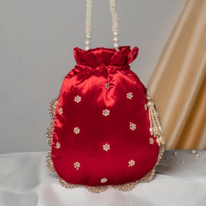 May include: A red velvet drawstring bag with a pearl handle and a beaded trim. The bag is decorated with gold floral embroidery.
