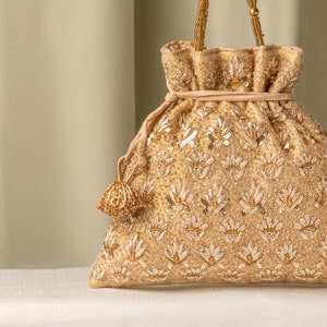 Op de afbeelding: Een gouden trekkoordtas met een bloemenpatroon en een kwast. De tas is gemaakt van een zachte, luxe stof en is perfect voor speciale gelegenheden.