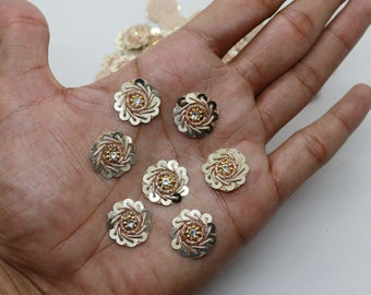 May include: Eight gold-tone flower-shaped embellishments with a clear rhinestone center. Each embellishment has a swirl design.