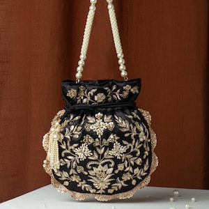 May include: Black satin handbag with gold floral embroidery and a scalloped edge. The bag features a pearl beaded handle and a tassel with pearl accents. The bag is approximately 8 inches tall.