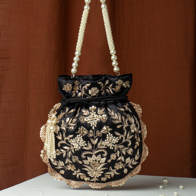 May include: Black satin handbag with gold floral embroidery and a scalloped edge. The bag features a pearl beaded handle and a tassel with pearl accents. The bag is approximately 8 inches tall.