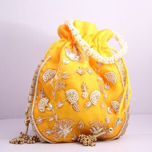 May include: A yellow drawstring bag with a pearl handle and gold embroidery. The bag has a tassel on each side.