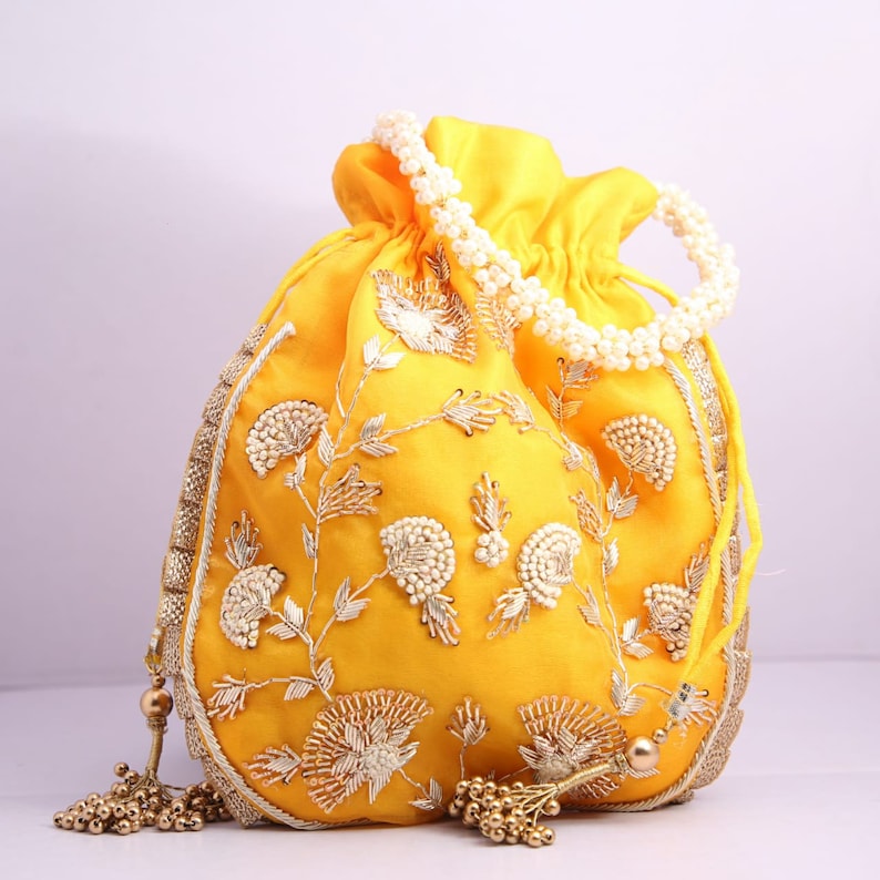 May include: A yellow drawstring bag with a pearl handle and gold embroidery. The bag has a tassel on each side.