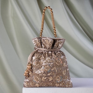 Könnte beinhalten: Ein brauner, bestickter Kordelzugbeutel mit Perlenhenkel und Quaste. Die Tasche hat aufwendige Blumenmuster aus Goldfaden und kleine, farbige Perlen. Die Tasche ist aus einem weichen, strukturierten Stoff gefertigt.