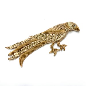 Può includere: Un'applicazione di uccello ricamata in oro con una lunga coda. L'uccello è in piedi su due gambe e ha un design dettagliato.