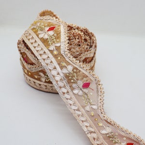 May include: A roll of beige embroidered trim with a scalloped edge. The trim features floral designs with red, pink, and green accents. The trim is made of a sheer fabric with a delicate texture.