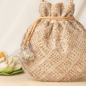 Peut inclure: Un sac à cordon de couleur crème avec un motif de perles dorées et un pompon. Le sac est fait d'un tissu doux et a une fermeture à cordon.
