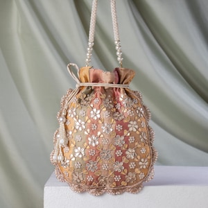 Könnte beinhalten: Ein bestickter Kordelzugbeutel mit einem perlenbesetzten Griff und Quaste. Die Tasche hat ein Blumenmuster mit goldenen und silbernen Akzenten. Die Farben der Tasche sind Gelb-, Rosa- und Grüntöne.