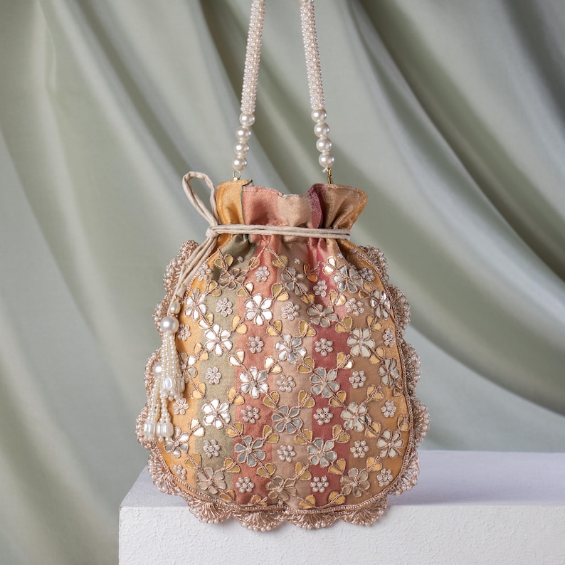 May include: A colorful, embroidered drawstring bag with a pearl beaded handle and tassel. The bag features a floral pattern with gold and silver accents. The bag's colors include shades of yellow, pink, and green.