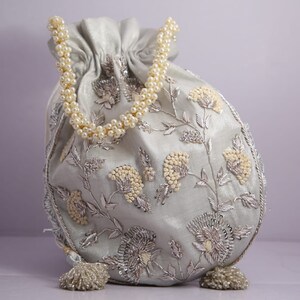 May include: A light blue drawstring bag with a pearl handle and silver floral embroidery.