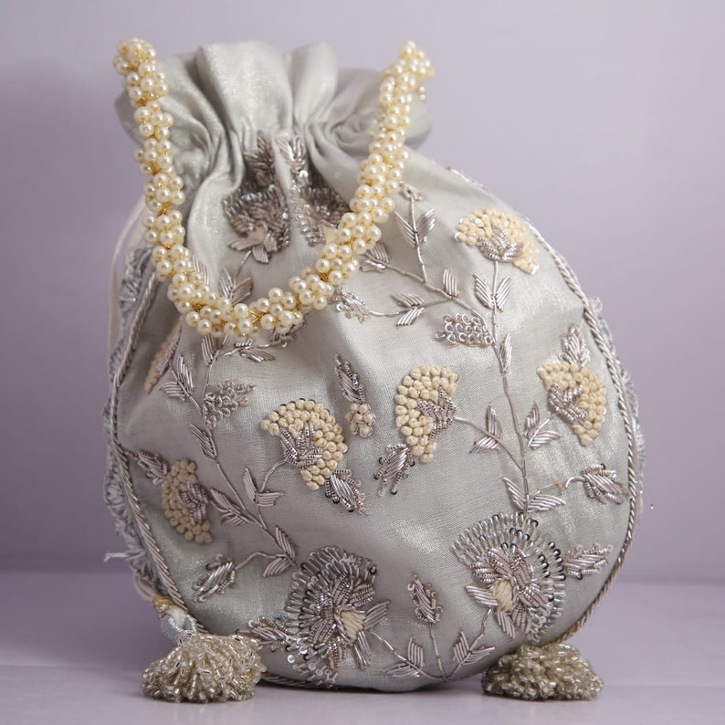 May include: A light blue drawstring bag with a pearl handle and silver floral embroidery.