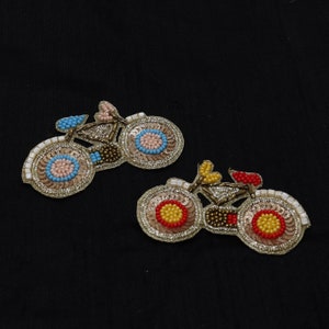 May include: Two beaded bicycle appliques, one with pink and blue beads and the other with red and yellow beads.