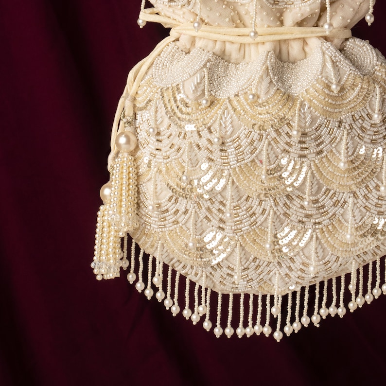 May include: A white beaded drawstring bag with a pearl tassel. The bag is decorated with a pattern of white and gold beads.