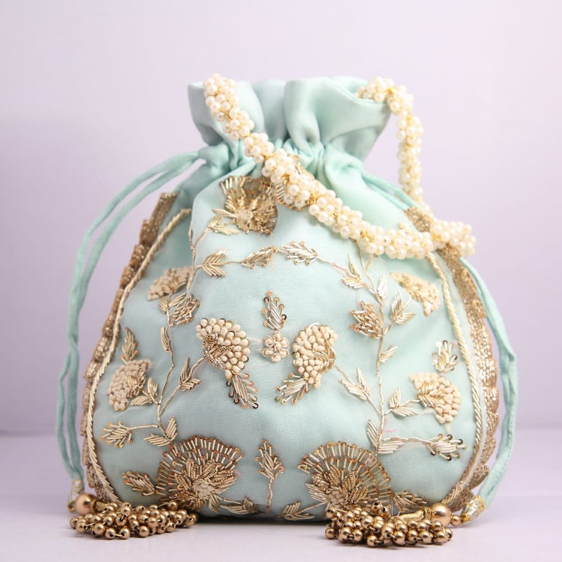 May include: A light blue drawstring bag with gold and white embroidery. The bag has a pearl chain handle and gold tassel accents.