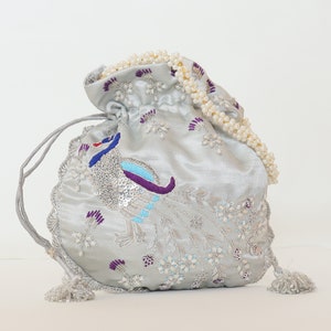 May include: A silver satin drawstring bag with a pearl trim and embroidered peacock design. The bag features sequins and colorful thread embroidery.