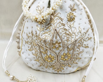 May include: A white drawstring bag with a pearl trim and gold embroidery. The bag features a floral design and is decorated with small pearls.