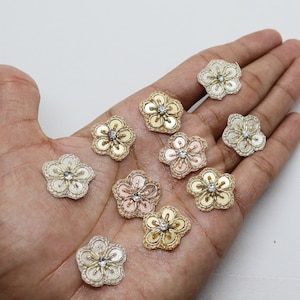 Può includere: Assortimento di dieci decorazioni a forma di fiore con paillettes e strass. Le decorazioni sono in tonalità oro, rosa e bianco.