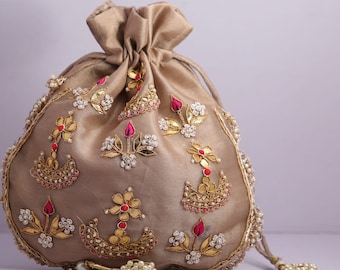 Könnte beinhalten: Eine goldene Kordeltasche mit aufwendigen Stickereien, die Blumenmuster, Perlen und Pailletten zeigen. Die Tasche hat eine rosa und rote Akzentfarbe.