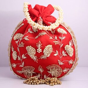 May include: A red drawstring bag with a pearl handle and gold embroidery. The bag is decorated with floral patterns and has a tassel.