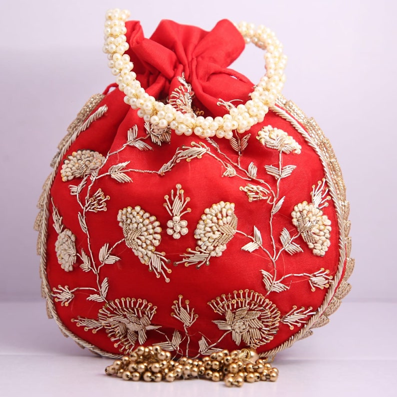 May include: A red drawstring bag with a pearl handle and gold embroidery. The bag is decorated with floral patterns and has a tassel.