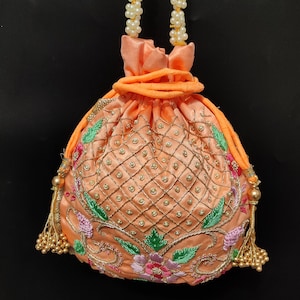 Puede incluir: Bolsa de cordón de color melocotón con asa de perlas y detalles de borlas doradas. La bolsa está bordada con diseños florales y un patrón de diamante.