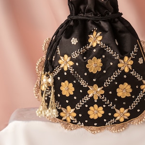 May include: A black velvet drawstring bag with gold and pearl embellishments. The bag is decorated with a floral pattern and has a tassel.