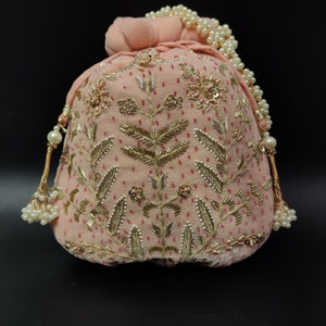 Puede incluir: Una bolsa de cord&oacute;n de terciopelo rosa con adornos dorados y de perlas. La bolsa est&aacute; decorada con un patr&oacute;n floral y tiene un borla de cuentas.