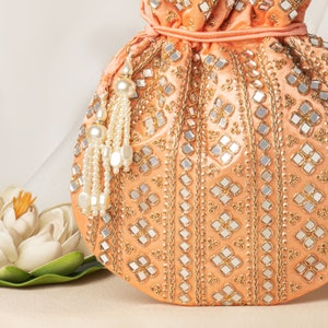 May include: Peach-colored drawstring bag with a beaded tassel. The bag is decorated with gold and silver mirror work in a geometric pattern.