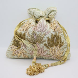 Könnte beinhalten: Eine hellgrüne Kordeltasche mit einem floralen Muster, das mit goldenen und rosafarbenen Fäden bestickt ist. Die Tasche hat einen goldenen Quasten und eine goldene Kordel.