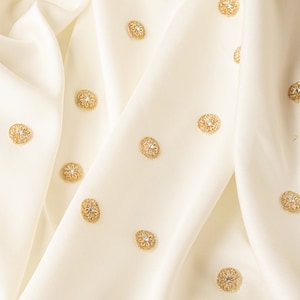Może przedstawiać: Biały materiał z złotymi okrągłymi ozdobami. Materiał jest złożony, a ozdoby rozrzucone po powierzchni.