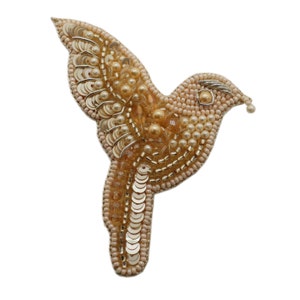 Può includere: Un broche a forma di uccello in perle dorate e crema con un design delicato. L'uccello è in volo con le ali spiegate. Il broche è fatto di piccole perle e paillettes.