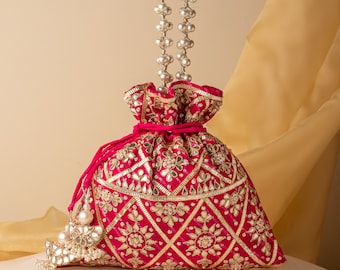 May include: A pink drawstring bag with a silver beaded strap and a silver tassel. The bag is decorated with gold embroidery and mirror work.