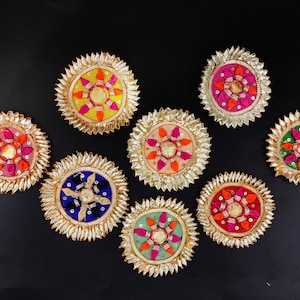 Op de afbeelding: Acht decoratieve ronde ornamenten met gouden randen en kleurrijke stoffen centra. De ornamenten zijn in verschillende kleuren, waaronder roze, oranje, groen, blauw en geel.