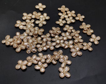 May include: A collection of gold-colored flower-shaped embellishments with a sparkly finish. The embellishments are made of fabric and have a delicate, intricate design.