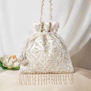 Può includere: Una borsa a cordoncino bianca con perline, con una tracolla a catena di perle e una frangia di perle. La borsa è decorata con un motivo di ricamo di perle e argento.