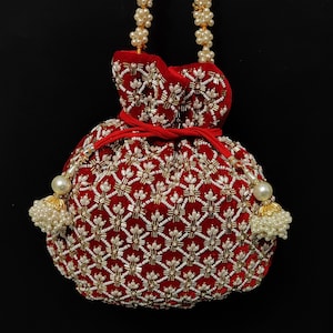 Könnte beinhalten: Eine rote Samt-Kordeltasche mit einem Perlen- und Goldperlenmuster. Die Tasche hat einen Perlen- und Goldperlenriemen.