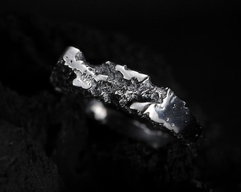 Può includere: Un anello d'argento con un design testurizzato e organico. L'anello è posizionato su uno sfondo nero.