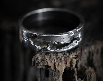 May include: A silver ring with a textured, broken design. The ring is sitting on a piece of weathered wood.